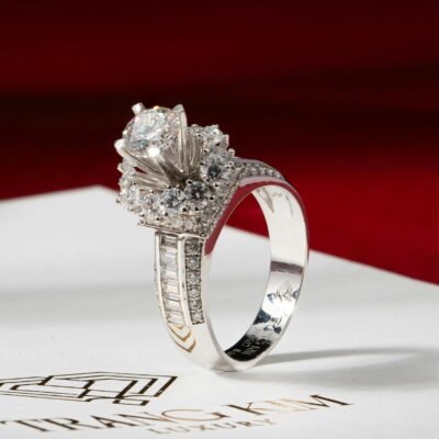 Close-up of a diamond ring with intricate setting resting on a white card against a luxurious red backdrop.