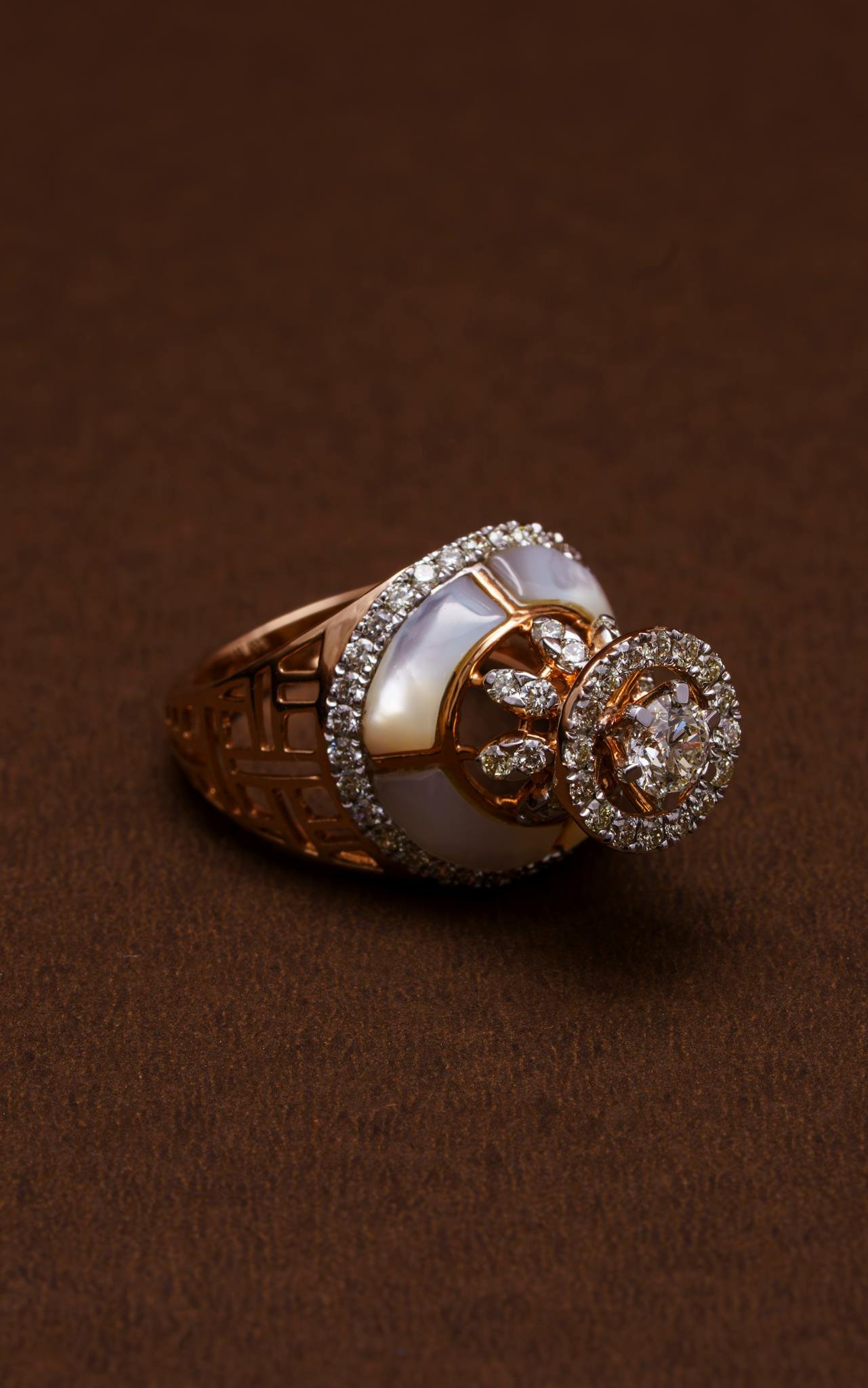 Luxurious gold ring with diamonds and pearl detail on a rich brown surface, showcasing elegance.